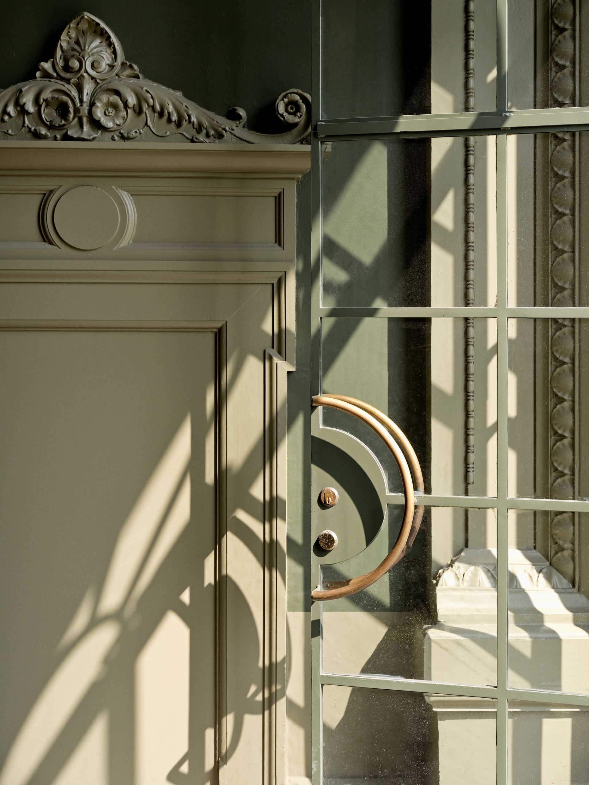 Close-up of a white door with ornate trim and a half-circle handle, next to a window with light and shadow.
