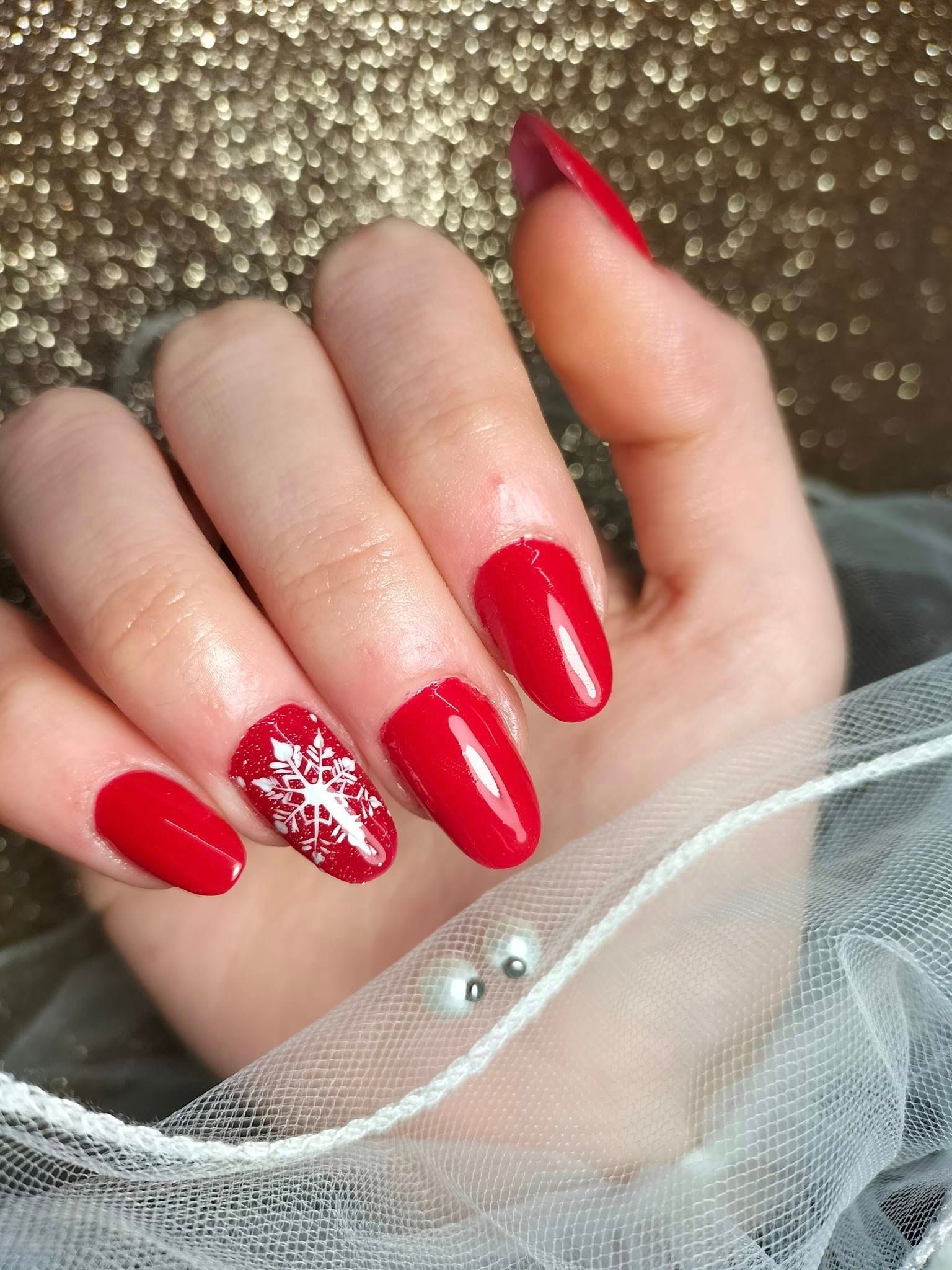 Un primer plano de la mano de una mujer con uñas rojas y un diseño de copo de nieve.