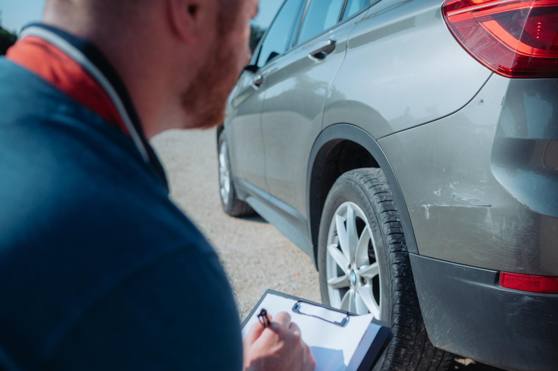 ein Mann mit Klemmbrett sieht sich den Schaden am Heck eines Autos an