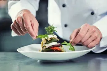 Ein Koch bereitet in einer Küche einen Teller mit Essen zu. Restaurant Ambiente