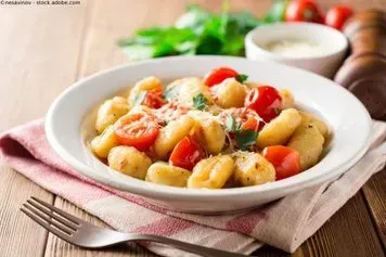 Eine Schüssel Gnocchi mit Tomaten und Käse auf einem Holztisch mit einer Gabel. Restaurant Ambiente