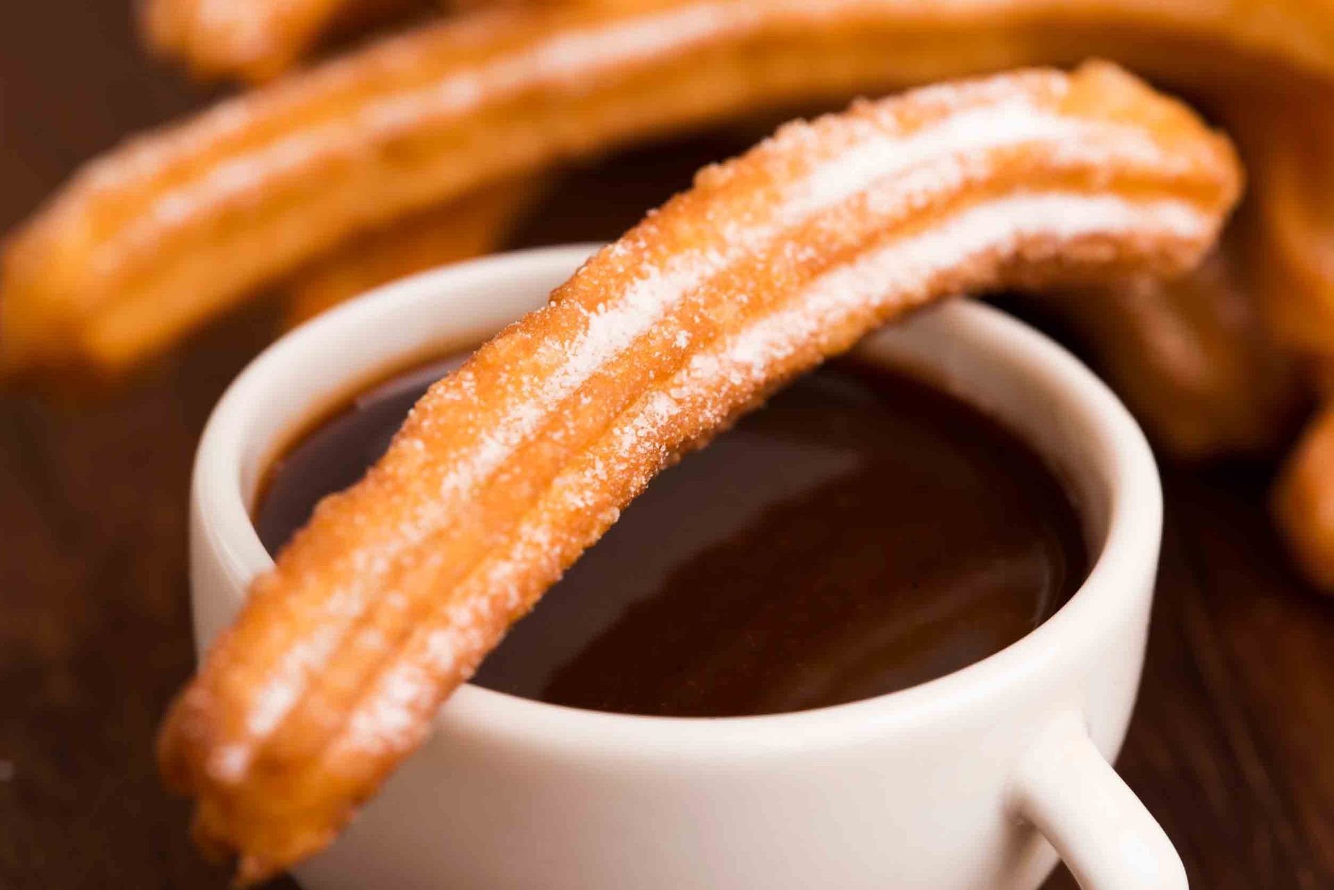 Un churro que sobresale de una taza de salsa de chocolate.