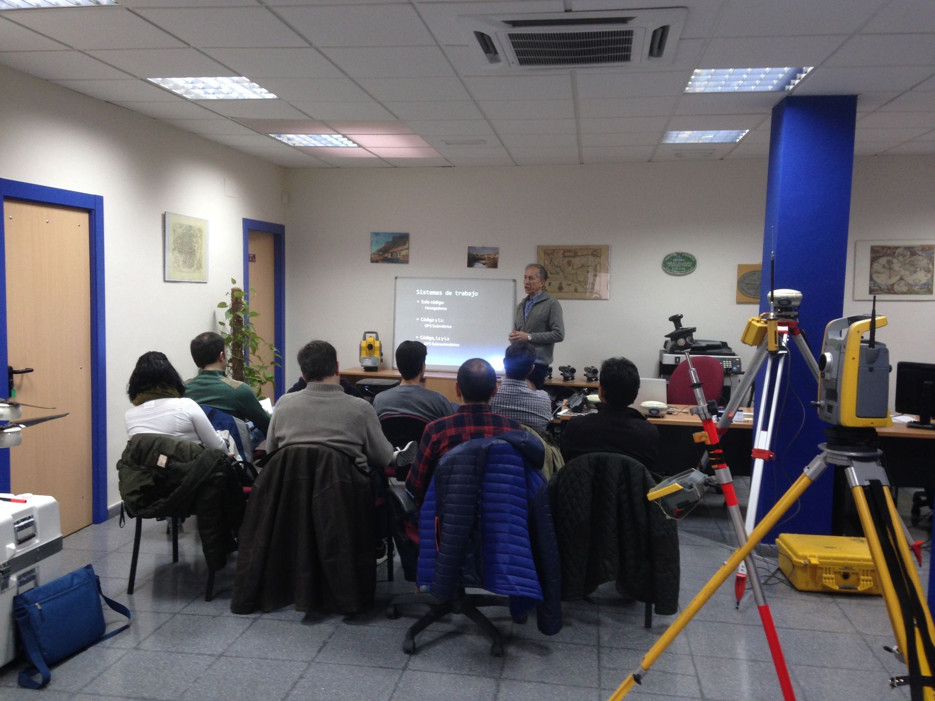 Obreros de la construcción con chalecos de seguridad y cascos. Dentro de un edificio, algunos revisando planos.
