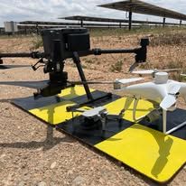Dos drones sobre tapetes amarillos y negros con paneles solares en el fondo.