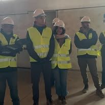 Obreros de la construcción con chalecos de seguridad y cascos. Dentro de un edificio, algunos revisando planos.