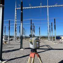 Un instrumento de medición sobre un trípode, delante de líneas y equipos de alta tensión.