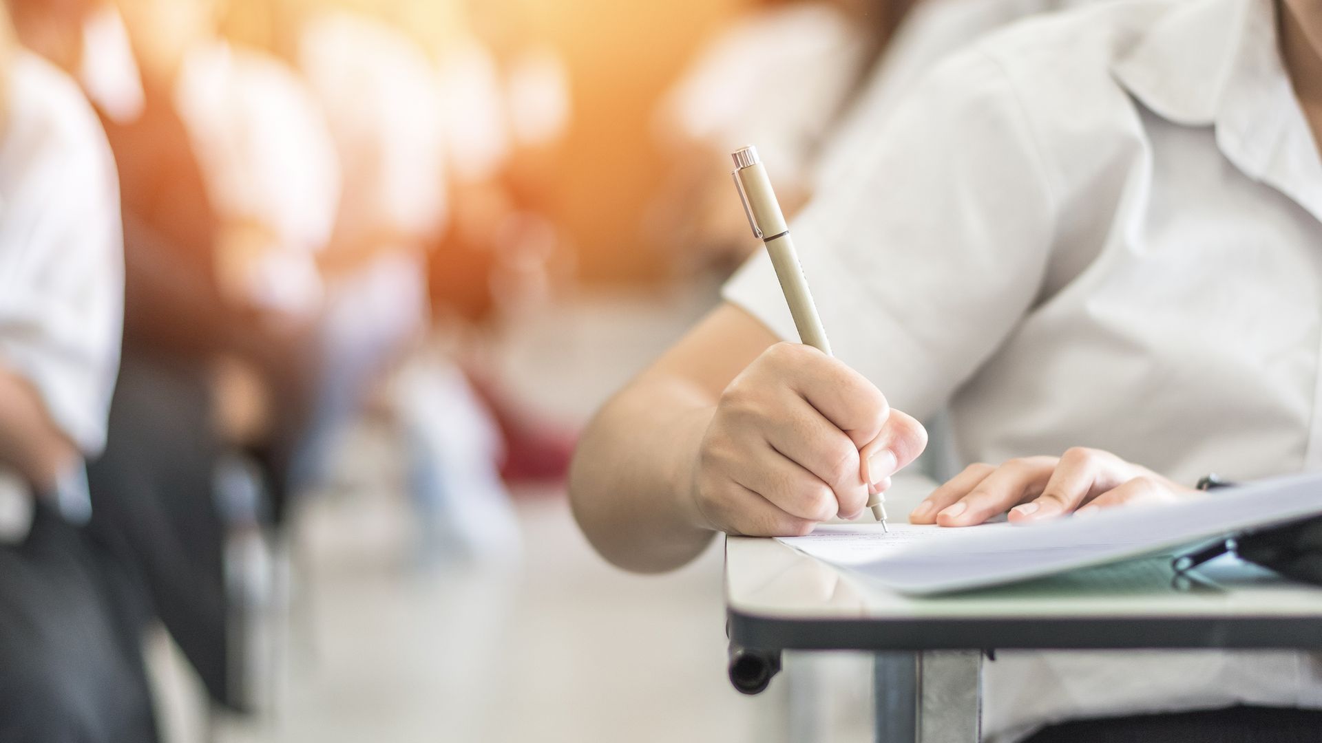 Una mujer está sentada en un escritorio escribiendo en un trozo de papel con un bolígrafo.