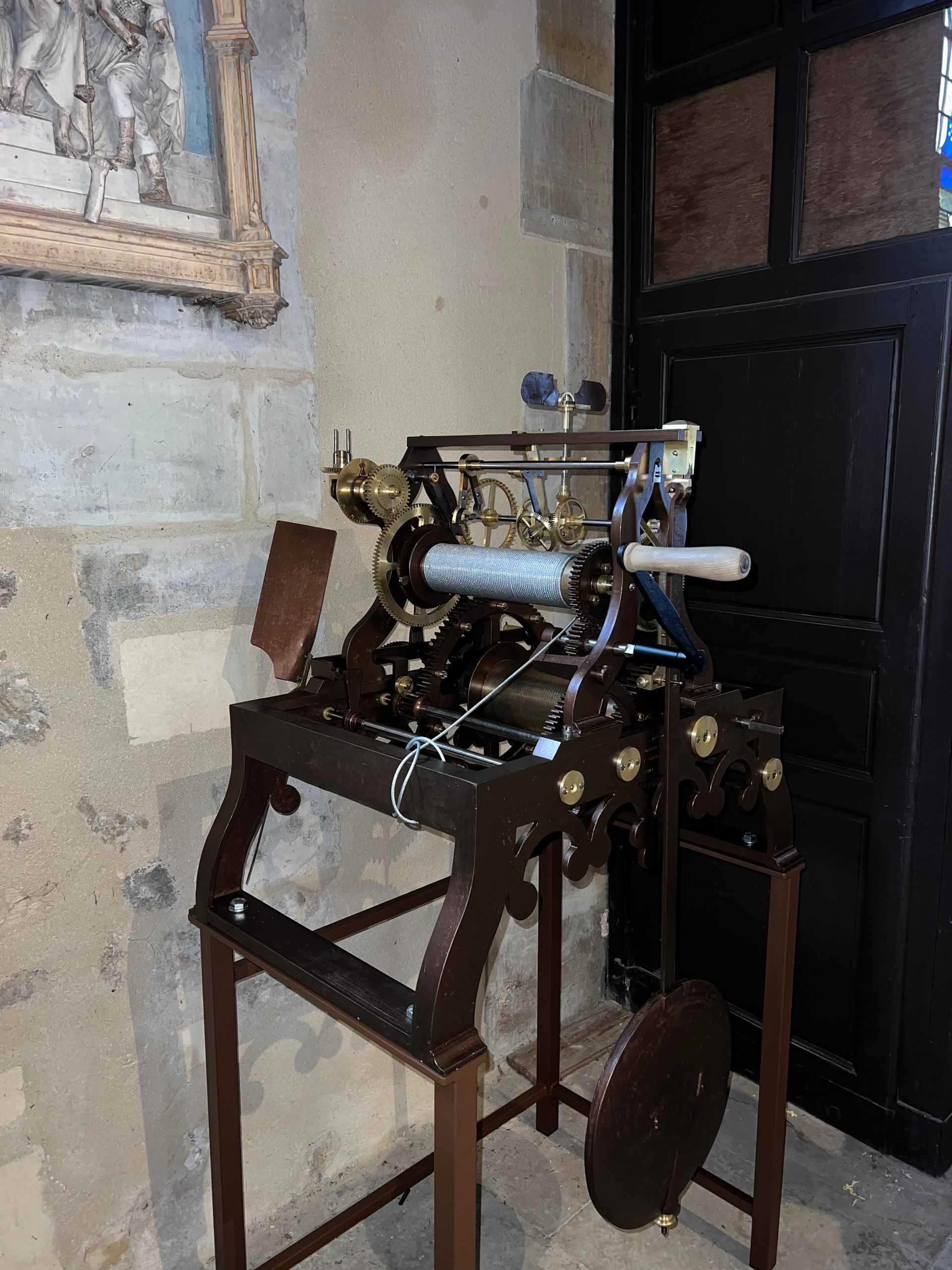 Une pendule d'édifice, montée sur un support à côté d'une porte noire dans une pièce aux murs de pierre.