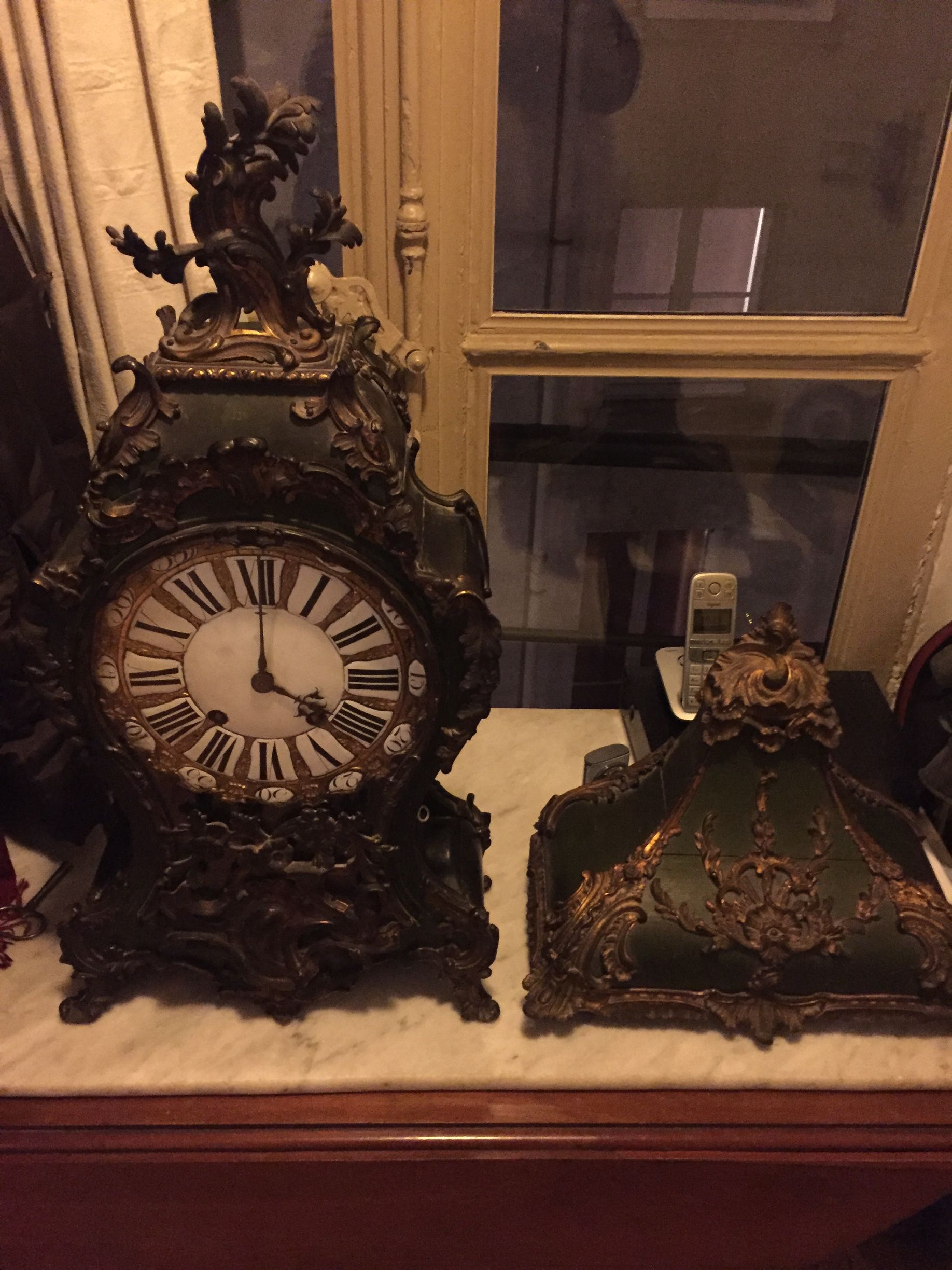 Horloge ancienne ornée de détails vert foncé et or, sur un plateau en marbre.