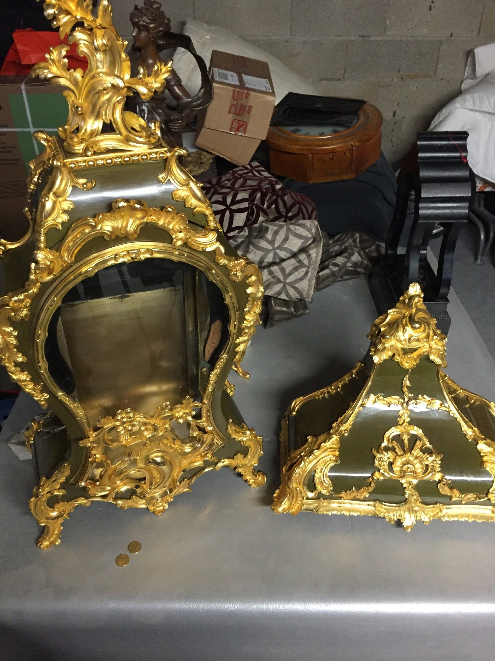 Boîtier d'horloge vert orné de dorures, avec couvercle amovible, posé sur une surface réfléchissante.