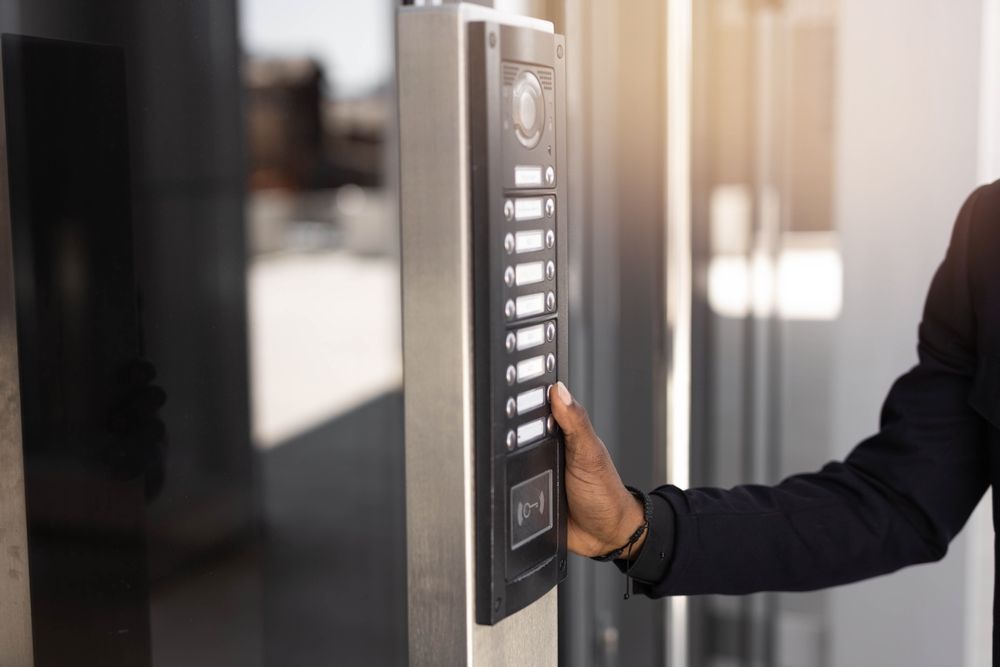 Una persona con traje utiliza un panel de intercomunicación con botones afuera de un edificio.