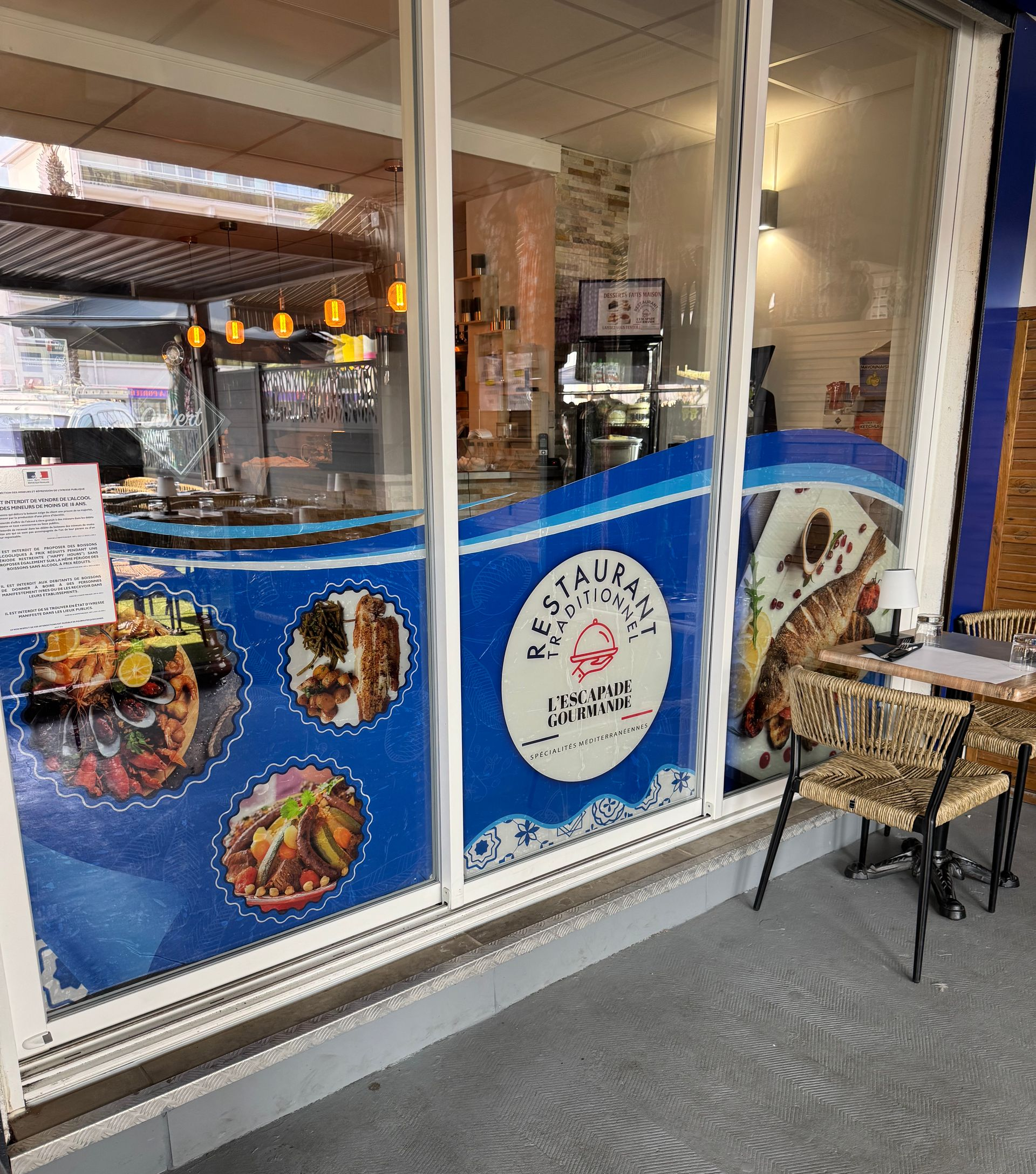 Devanture de restaurant avec signalisation bleue et blanche, photos de plats et sièges extérieurs.
