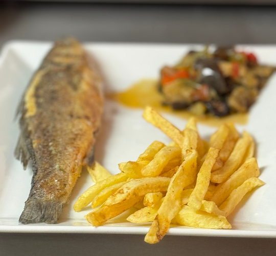 Poisson frit avec frites et légumes sur une assiette blanche.