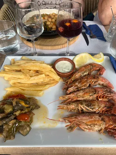 Assiette de crevettes grillées, frites et légumes avec une sauce, des boissons et d'autres aliments.