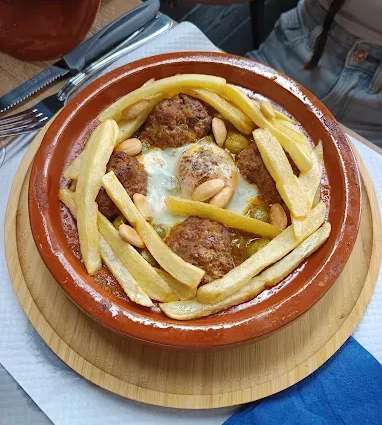 Plat avec boulettes de viande, œuf au plat, frites et amandes dans un bol en terre cuite sur une assiette en bois.
