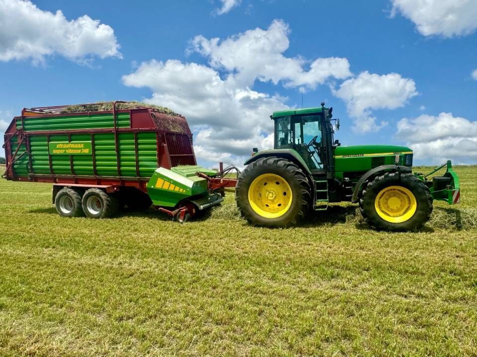 Un tracteur John Deere vert tire une remorque à travers un champ, sous un ciel bleu.