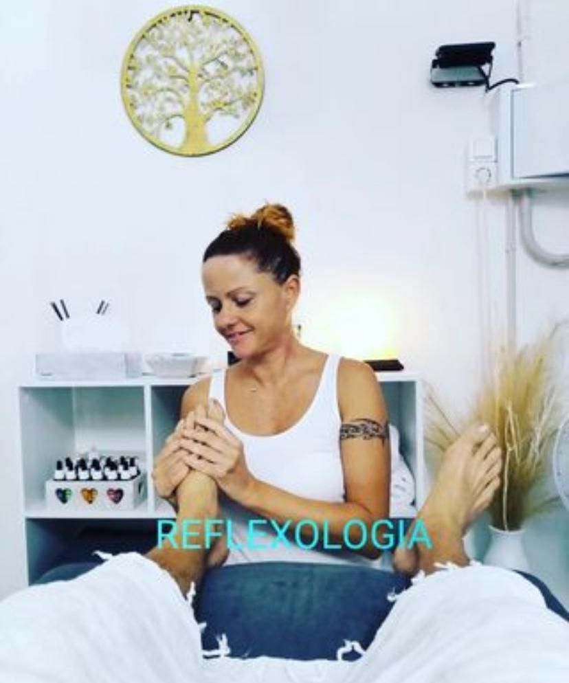 Dona fent tractament de reflexologia podal. Ambient blanc, art d'arbre, olis essencials visibles.