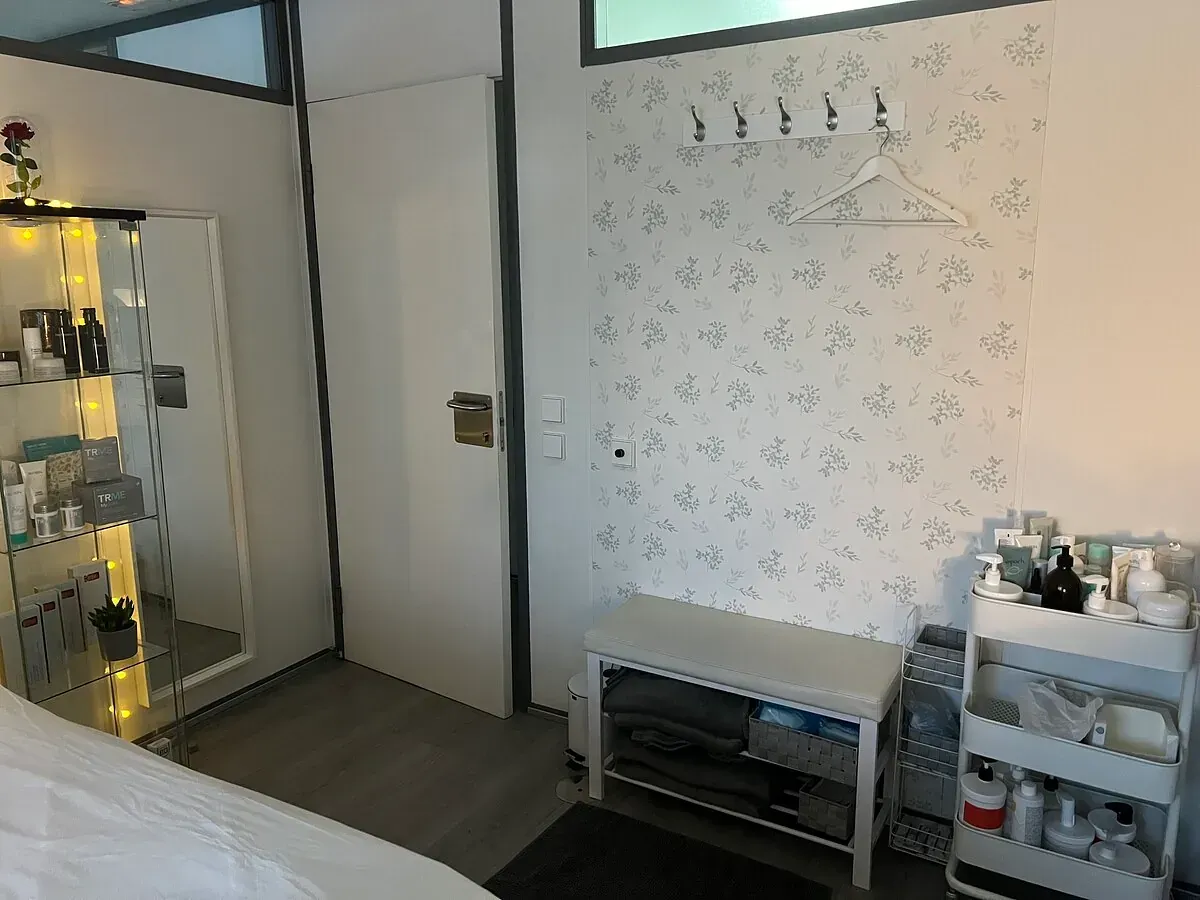 Una habitación con una cama, un espejo, un banco y un estante lleno de cosméticos.