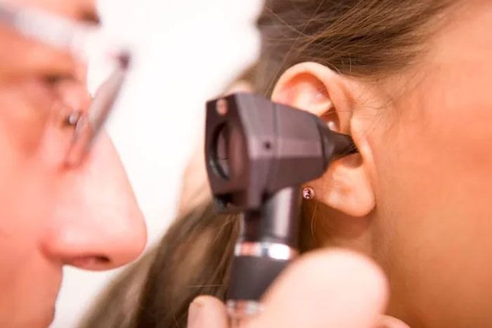 Un médico está examinando la oreja de una mujer con un otoscopio.