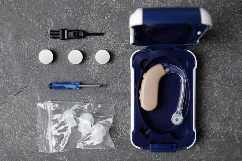 Un audífono en un estuche con un destornillador y tapones para los oídos.