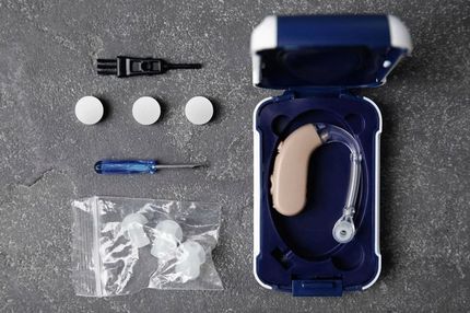Un audífono en un estuche con un destornillador y tapones para los oídos.