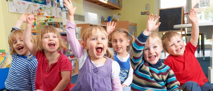Un grupo de niños levanta las manos en el aire en un aula.