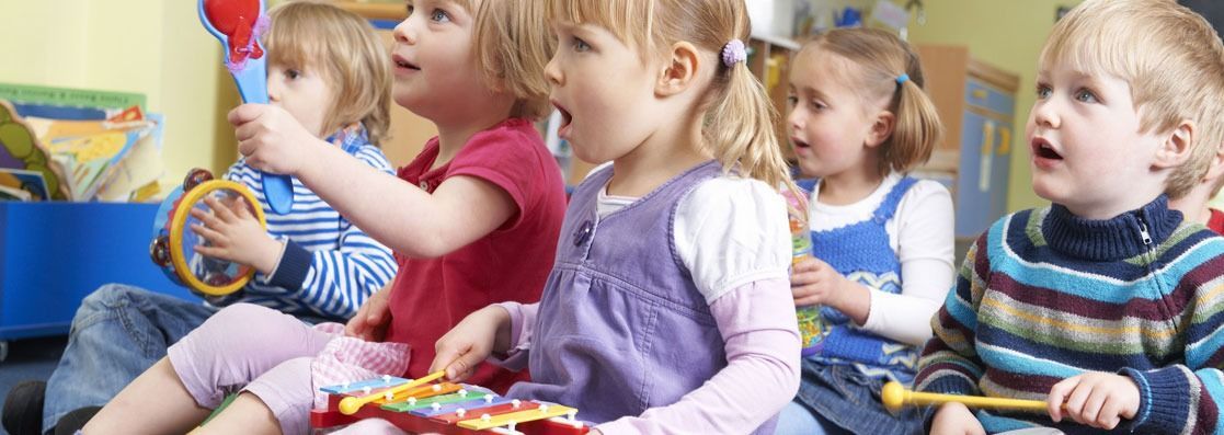 Un grupo de niños está sentado en el suelo tocando instrumentos musicales.