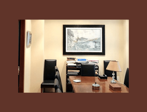 Interior de oficina con escritorio, sillas, obras de arte y lámpara.