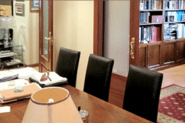 Una mesa de madera con tres sillas negras está frente a una puerta. Una lámpara se encuentra en primer plano.