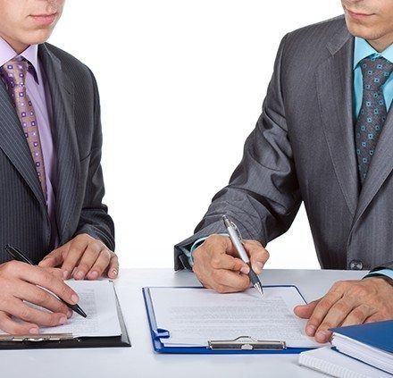 Dos hombres de traje firmando documentos en una mesa blanca.