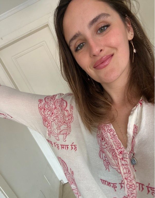 Mujer con blusa blanca con diseño rojo, sonriendo, en interiores.