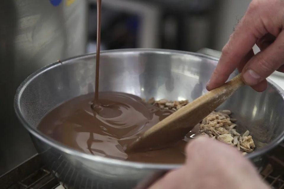 Une personne verse du chocolat dans un bol en métal avec une cuillère en bois.