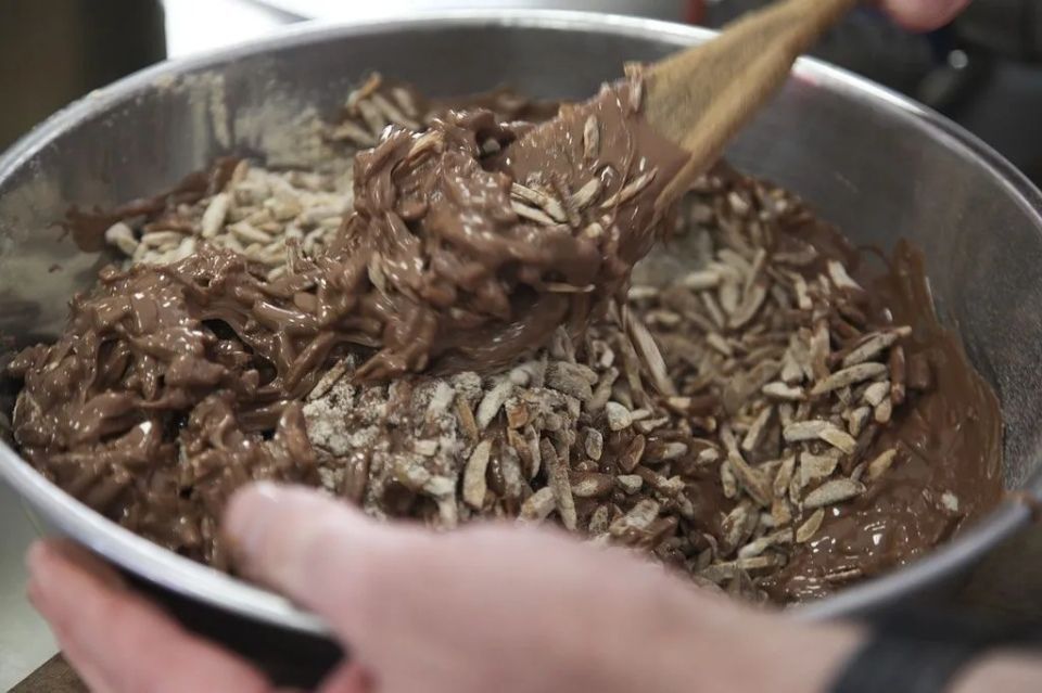 Une personne mélange du chocolat et des amandes dans un bol avec une cuillère en bois.
