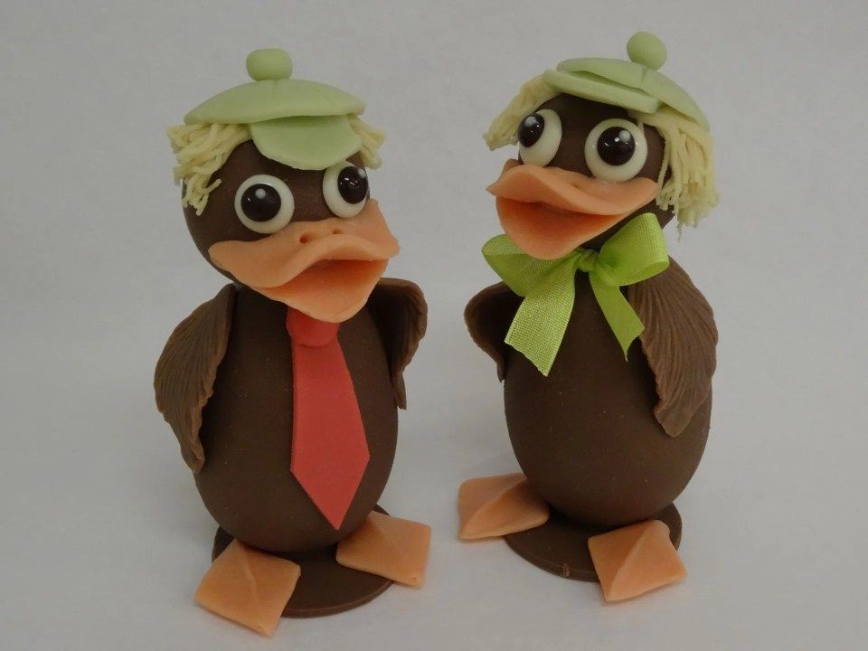 Deux canards en chocolat portant des chapeaux et des cravates se tiennent l'un à côté de l'autre