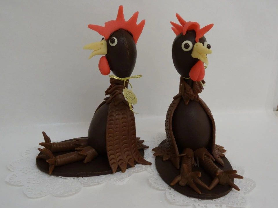 Deux poulets en chocolat sont assis l'un à côté de l'autre sur une surface blanche