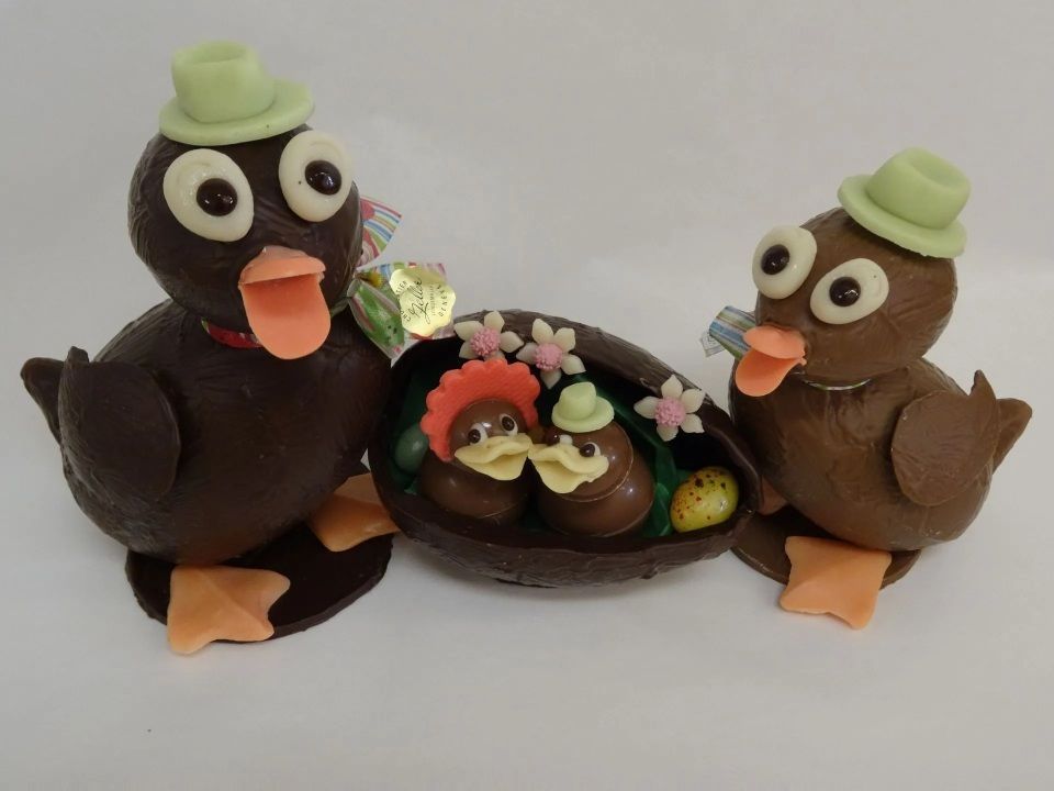 Deux canards en chocolat sont assis à côté d'un œuf de Pâques en chocolat