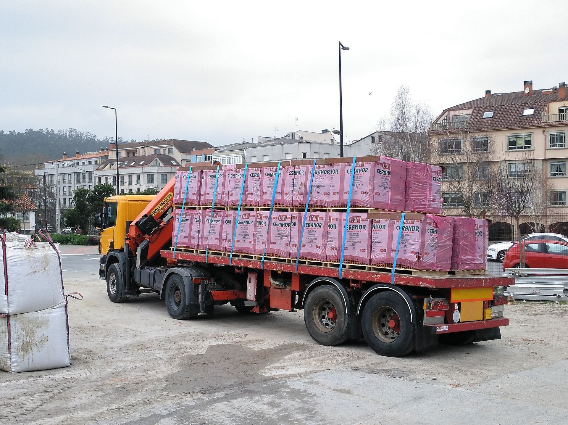 Un camión rojo transporta una pila de ladrillos rosas.