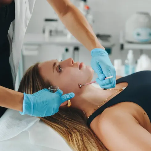 Tratamiento estético en el cuello de un cliente en una clínica, con manos enguantadas y un pequeño instrumento.