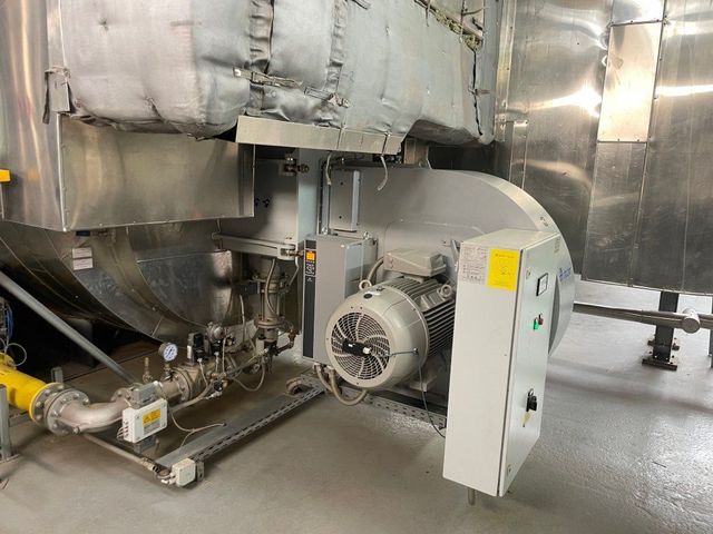 Industriekesselanlage mit einem großen Metallzylinder, einem angeschlossenen Elektromotor und einem Schaltkasten auf grauem Boden.