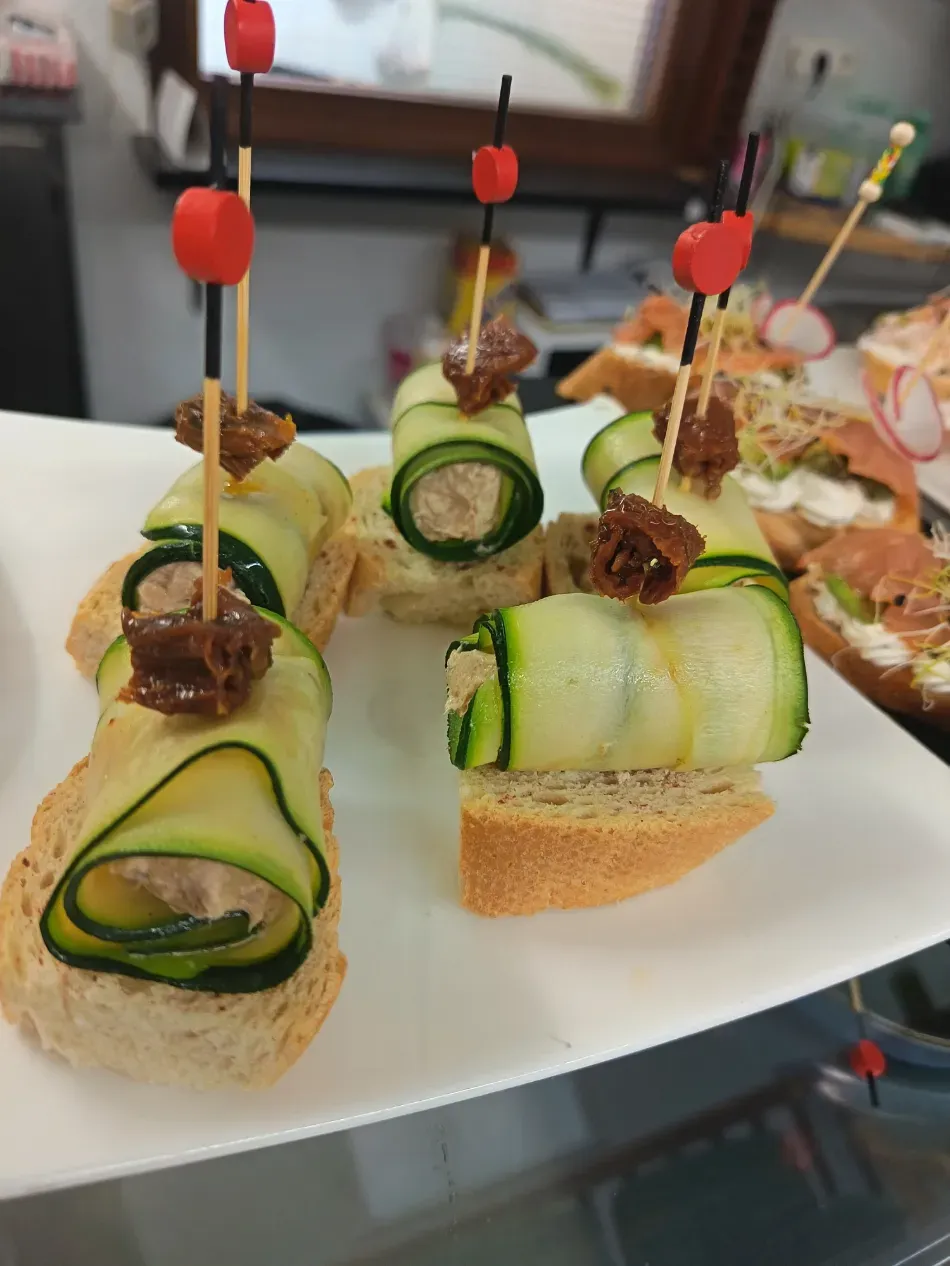 Rollitos de pepino y calabacín sobre pan, decorados con brochetas y guarnición, en un plato blanco
