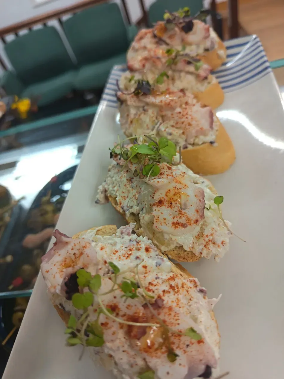 Rollos de sushi emplatados, cubiertos de hierbas y especias, en una fuente rectangular blanca sobre una mesa de restaurante
