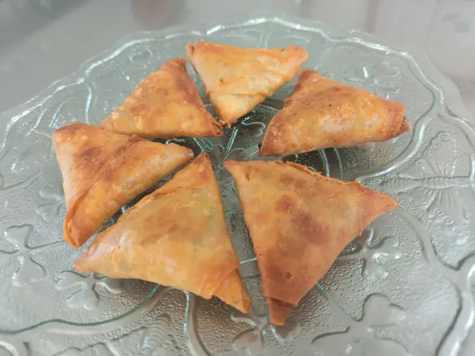 Seis samosas doradas dispuestas en un plato de vidrio transparente