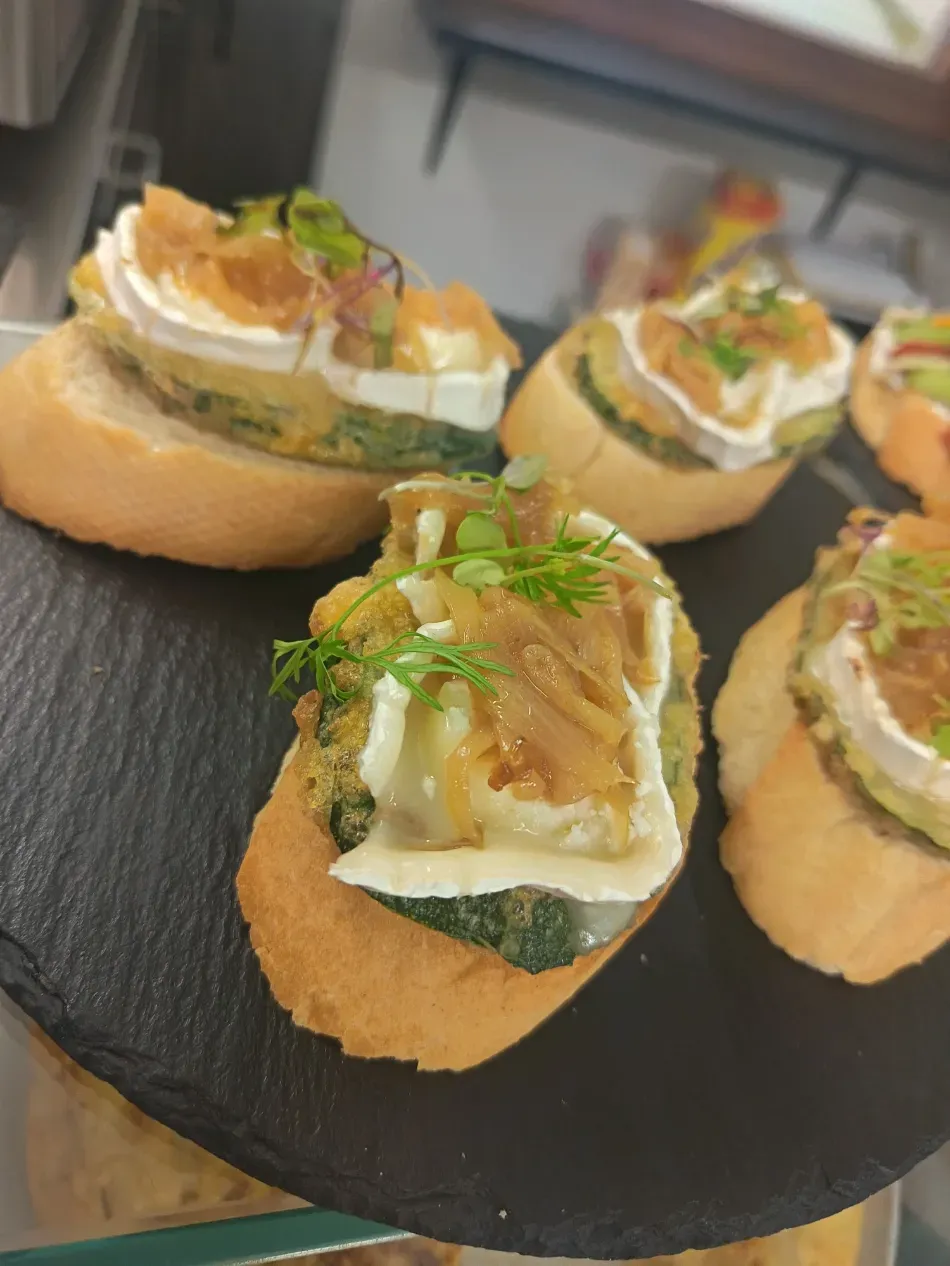 Bocaditos de pan artesanal con una cremosa cobertura y hierbas, servidos en una bandeja negra