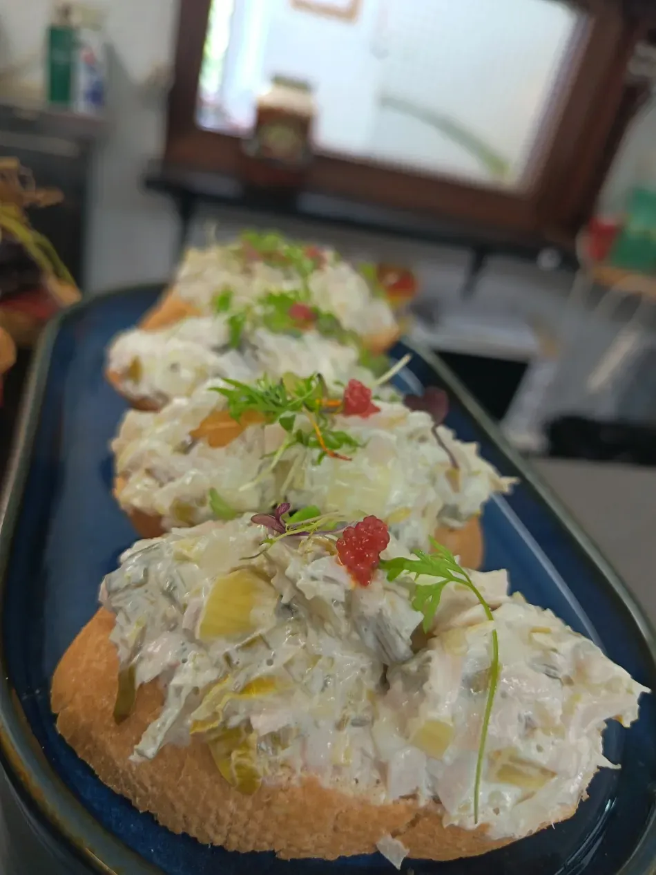 Canapés abiertos con ensalada cremosa, hierbas y un toque rojo, sobre una bandeja azul