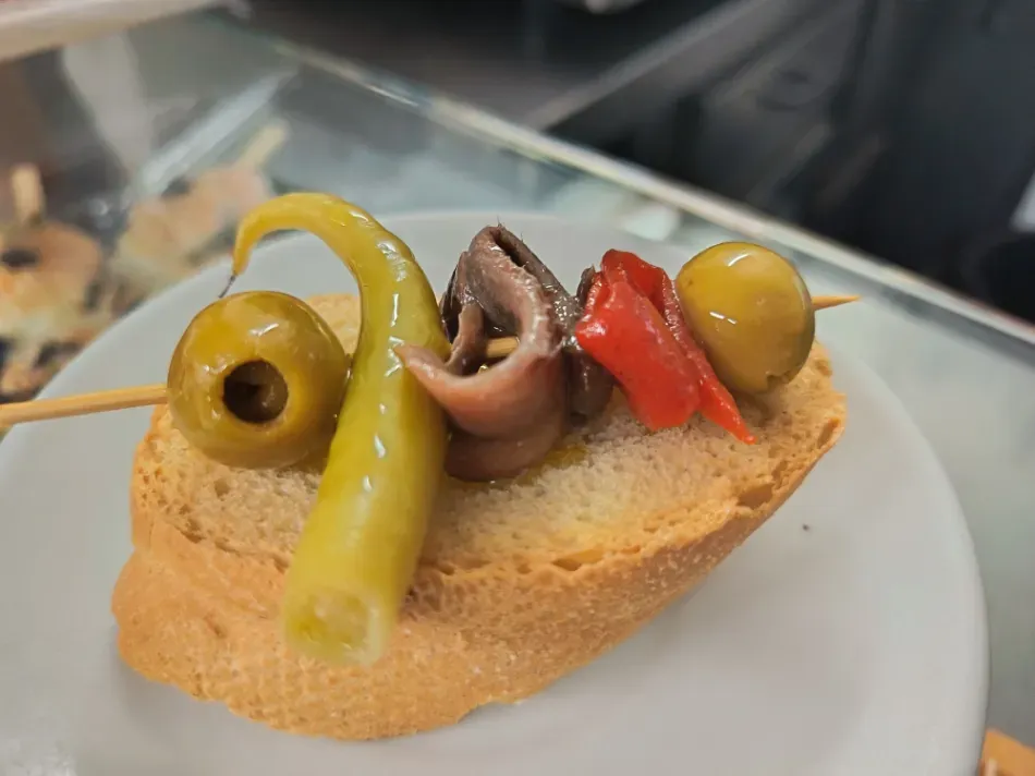 Brocheta de tapas con aceitunas, pimientos y calamar sobre una rebanada de pan en un plato blanco