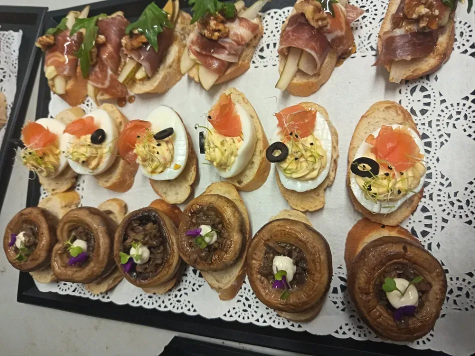 Una selección de aperitivos gourmet en porciones pequeñas, dispuestos en una bandeja decorativa: crostini, canapés y champiñones rellenos.