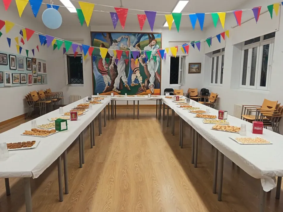 Salón de fiestas con largas mesas de buffet, guirnaldas de banderines de colores y un mural en la pared del fondo