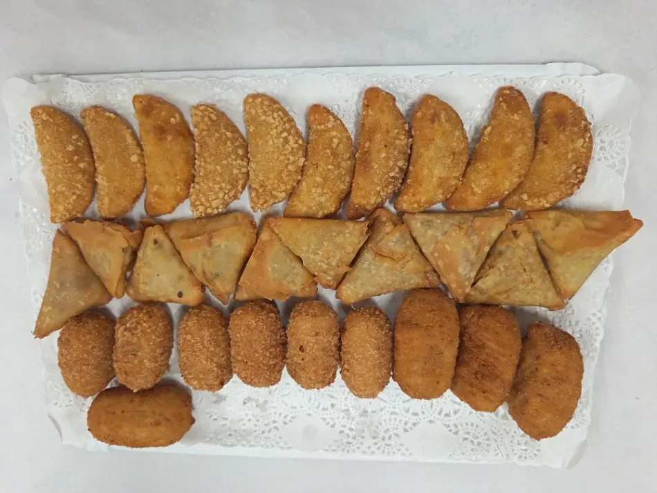 Pastelitos fritos dorados variados, dispuestos en filas sobre una bandeja forrada con papel