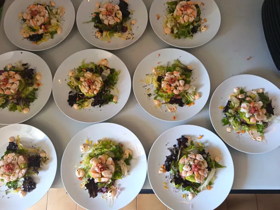 Varios platos blancos con ensalada verde y acompañamientos rosados, dispuestos sobre una mesa