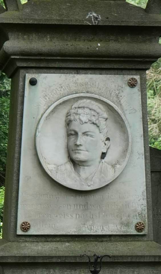 Gedenktafel aus Stein mit einem eingemeißelten runden Porträt einer Person und darunterliegender Inschrift.